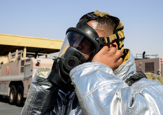 Senior Airman Dashawn Gilford, 379th Expeditionary Civil Engineer Squadron firefighter, dons his self-contained breathing apparatus face piece prior to operating a hand line from Engine 21 June 24, 2016, at Al Udeid Air Base, Qatar. There is more than one fire station here to provide adequate coverage and quick response time based on the geography of the base and volume of calls. (U.S. Air Force photo/Senior Airman Janelle Patiño/Released)