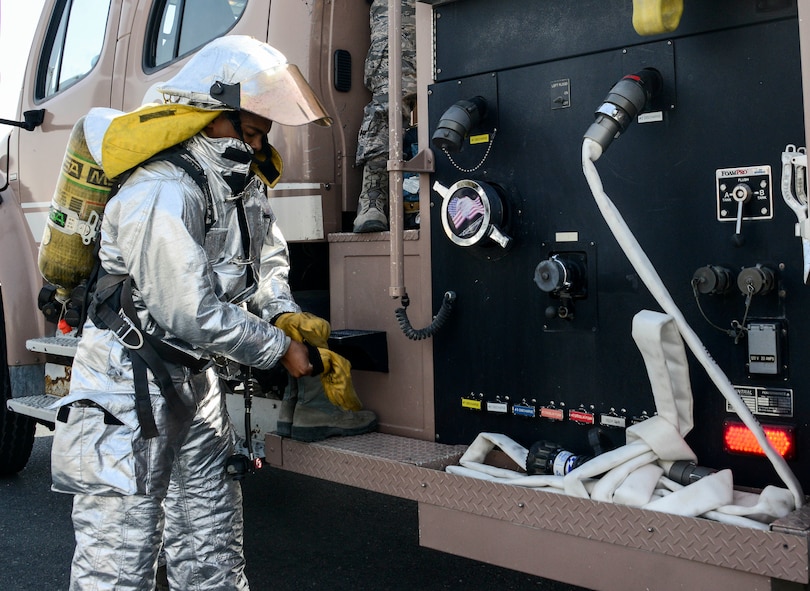 Senior Airman Dashawn Gilford, 379th Expeditionary Civil Engineer Squadron firefighter, dons his personal protective equipment prior to stretching a 1 ¾-inch hand line from the side of the Engine 21 June 24, 2016, at Al Udeid Air Base, Qatar. Firefighters place their personal protective equipment onto the fire truck and inspect their self-contained breathing apparatus in preparation for each work shift. Fire truck operators also inspect and start the truck to ensure the vehicle is ready for service and nothing is broken or missing. (U.S. Air Force photo/Senior Airman Janelle Patiño/Released)