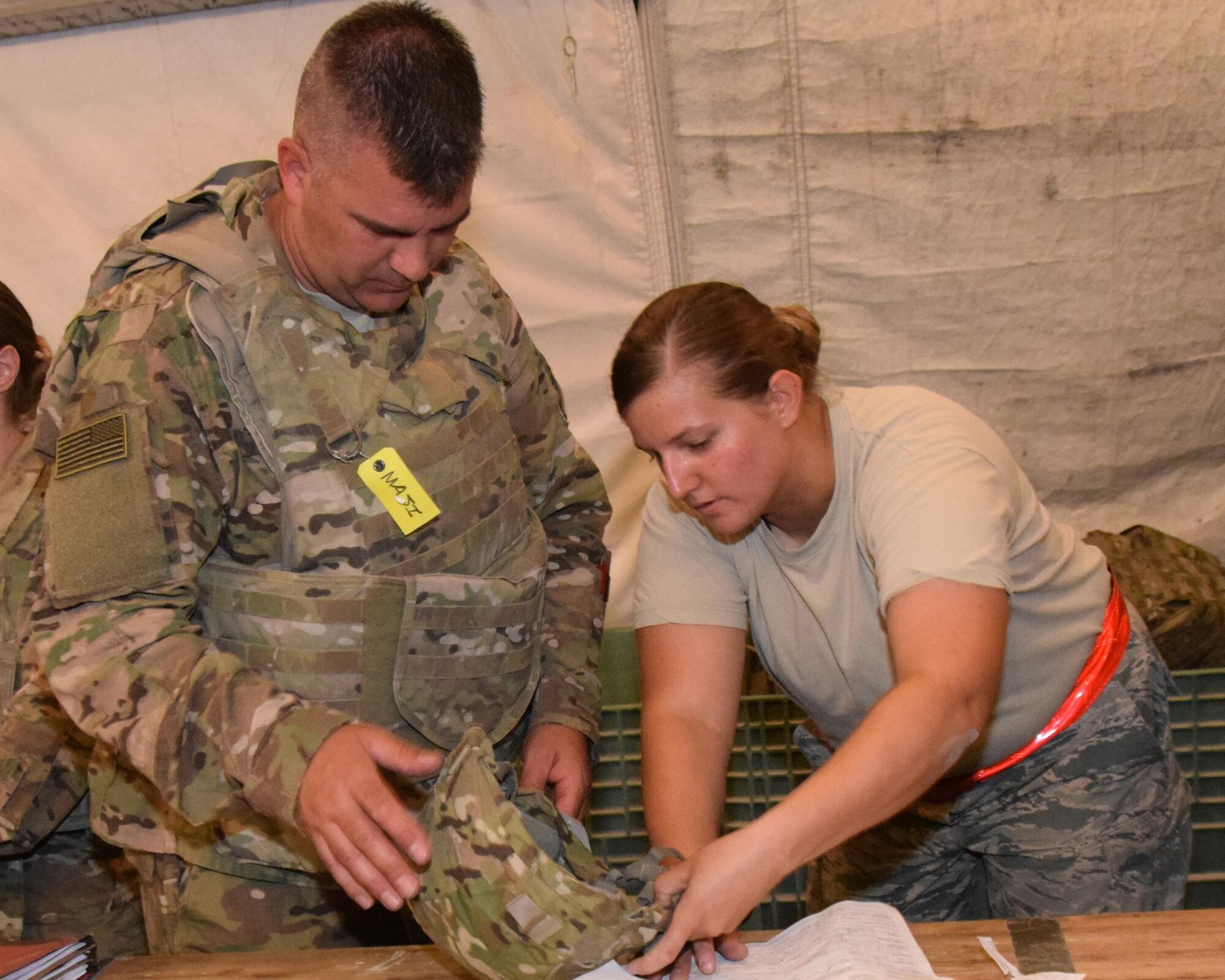 Staff Sgt. Kendra McAlpin, s supervisor with the 379th Expedtionary Logistics Readiness Squadron,  assists an Airman heading downrange with the fit of his helmet and paperwork June 23, 2016 at Al Udeid Air Base, Qatar. McAlpin works in the Expeditionary Theater Distribution Center insuring Airmen are equipped with properly fitting body armor before they contimue their journey to the AOR.  (U.S. Air Force photo/Technical Sgt. Carlos J. Trevino/Released)