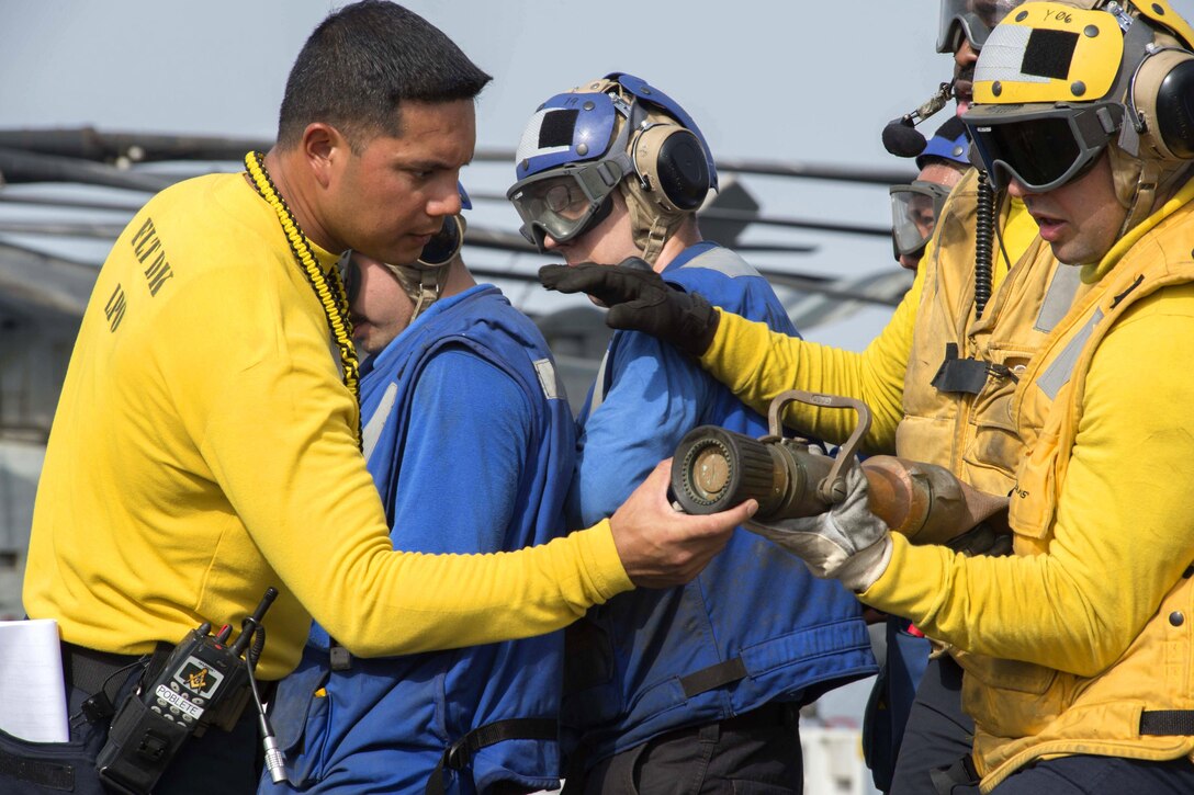 Navy Petty Officer 1st Class Mark Poblete instructs sailors on proper hose handling during an aircraft fire drill on the flight deck of the amphibious assault ship USS Boxer in the Arabian Gulf, July 5, 2016. Poblete is an aviation boatswain’s mate handling. Navy photo by Petty Officer 2nd Class Debra Daco