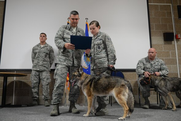 Lt. Col. Ian Dinesen, commander of the 55th Security Forces Squadron, and Senior Airman Kathryn Malone, a dog handler with the 55th SFS, read a meritorious service certificate for military working dog Ada at a military working dog retirement ceremony June 28, 2016. Ada is being retired at age 10, and adopted by Malone. (U.S. Air Force photo/Zach Hada)