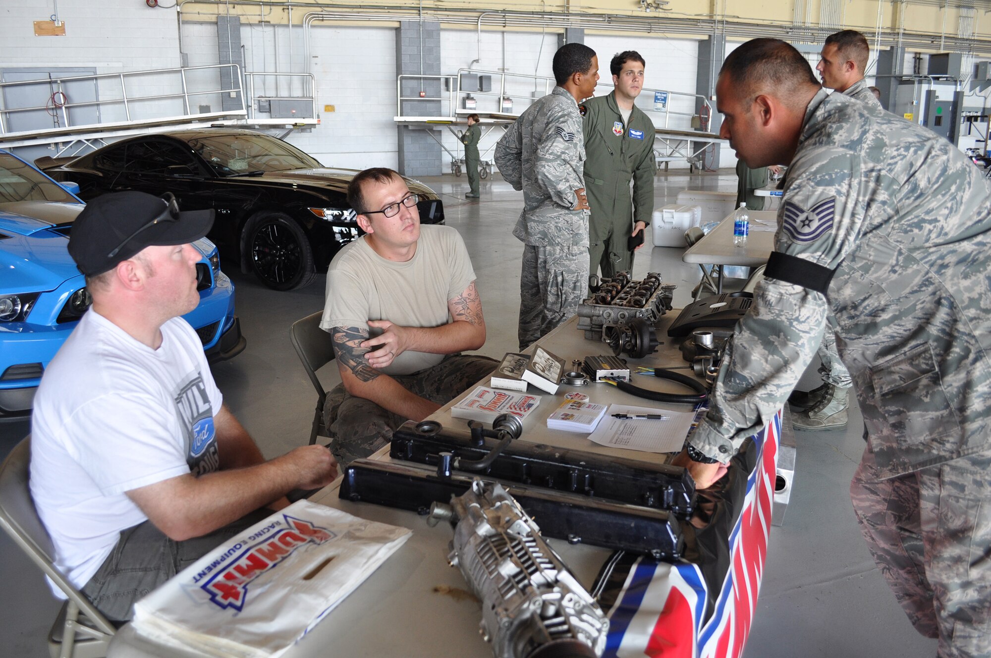 Tinker Car Club mentors Tech. Sgt. Brian Green, 513th Maintenance Squadron, and Senior Airman Justin Hunt, 552nd Maintenance Squadron, talk cars with Tech. Sgt. Eric Brambila, 552nd Aircraft Maintenance Squadron, during the “Bringing America’s Wing and Team Tinker Together Club Day” held June 27 in Dock 2 of Hangar 230. Nearly 500 people attended the event which featured 10 food trucks and music from America’s Wing Band. (Air Force photo by Ron Mullan/Released)
