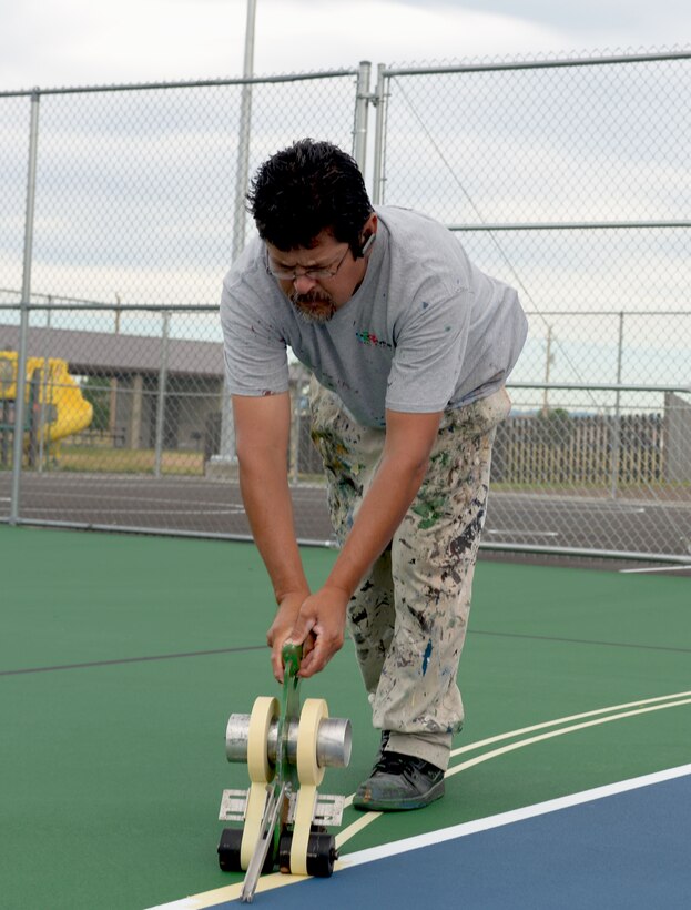 Ruben Reyes, Renner Sports Surfaces foreman, outlines painting areas for the multi-purpose sport courts at Ellsworth Air Force Base, S.D., June 14, 2016. The court can be used for different activities including tennis, basketball and volleyball, each requiring its own set of lines. (U.S. Air Force photo by Airman Donald Knechtel/Released) 