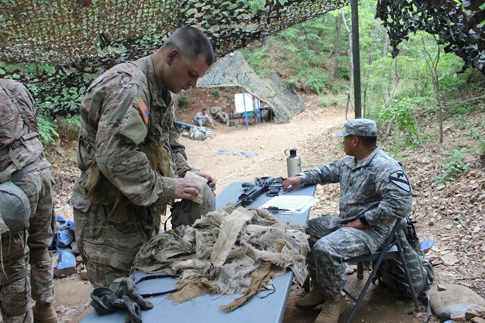 Spc. Jacob White, Co. A, 2nd Battalion, 8th Cavalry Regiment "Stallions," 1st Armored Brigade Combat Team, 1st Cavalry Division, prepares to camouflage his advanced combat helmet with materials provided by this EIB testing station at Camp Casey, South Korea. At this station, candidates are required to successfully camouflage their ACH, uniform, and face in under ten minutes. 