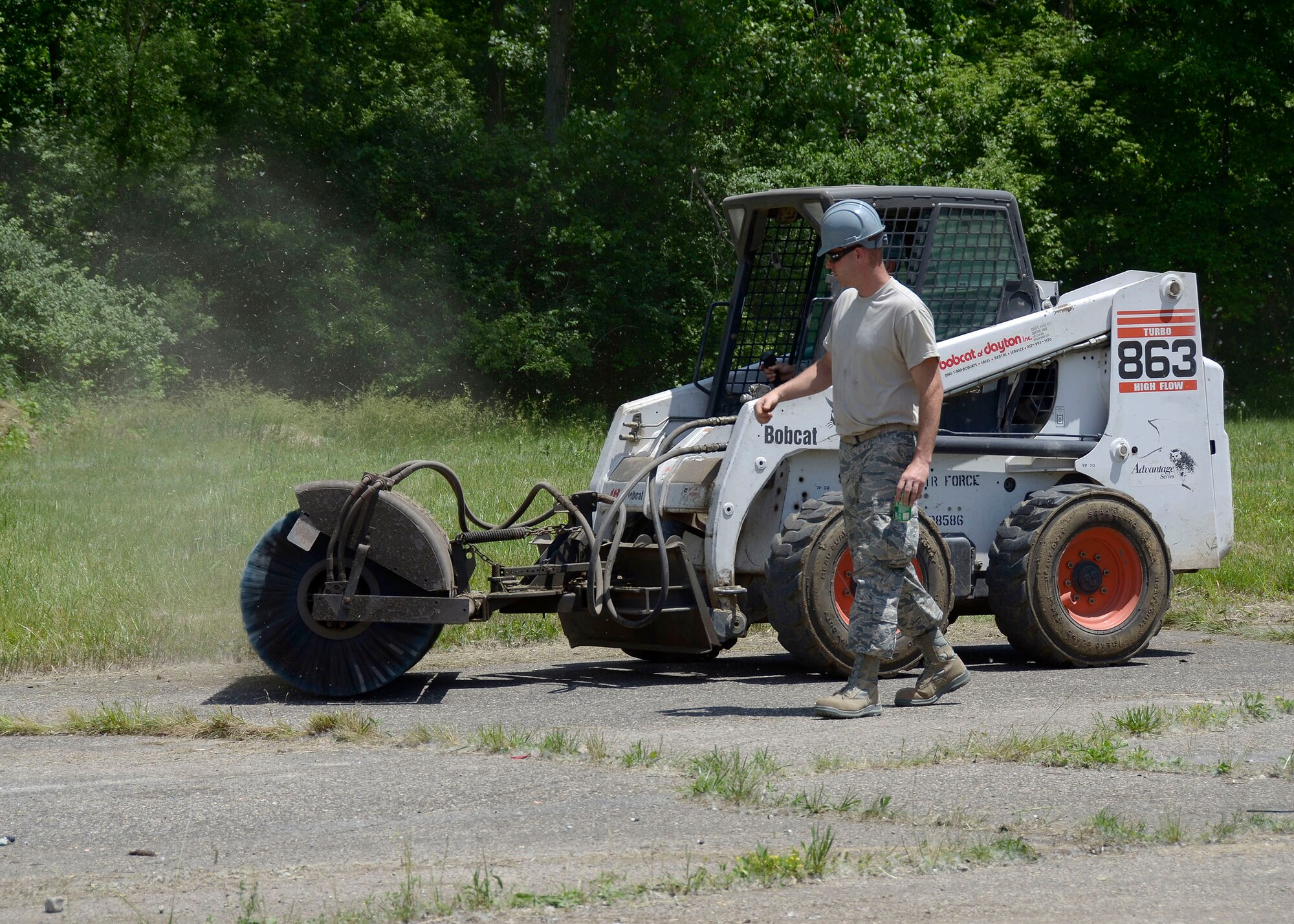 Senior Airman Luke Stewart, a heavy equipment operator for 445 CES, walks alongside a Bobcat as he instructs a fellow Airman on sweeper attachments operation June 3, 2016, at the Warfighter Training Center here. The sweeper attachment for the Bobcat is used frequently used to clean debris off of large surfaces such as Air Fields. (U.S. Air Force photo/Senior Airmen Joel A. McCullough)