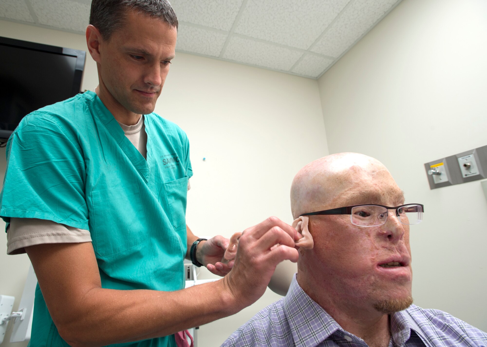 Maj. Stephen Cherrington (left), 59th Dental Group maxillofacial prosthodontist, compares retired Army Master Sgt. Todd Nelson’s prosthetic ear with new ears at the San Antonio Military Medical Center, Joint Base San Antonio-Fort Sam Houston, Texas, June 28. (U.S. Air Force photo/Staff Sgt. Kevin Iinuma)