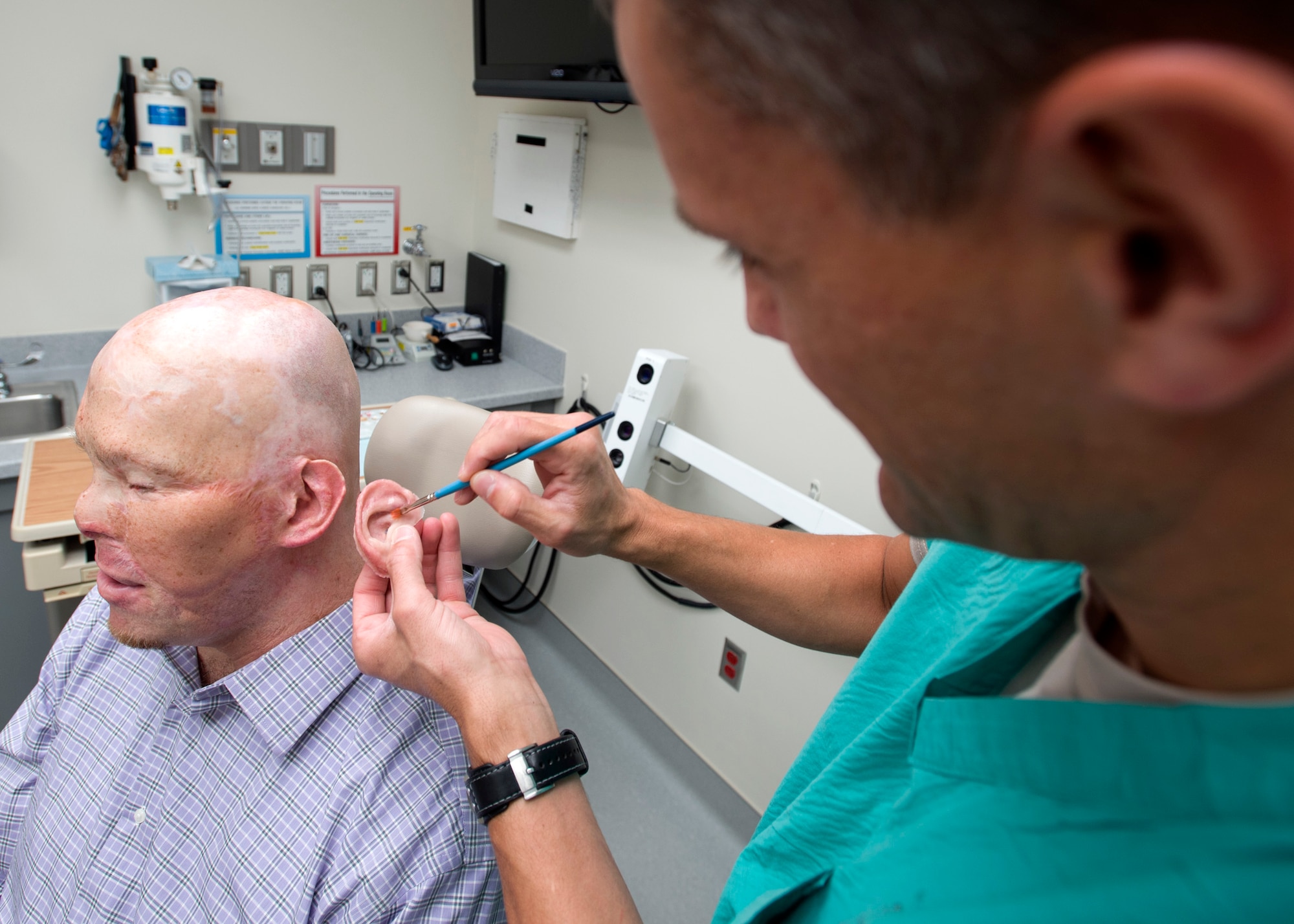 Maj. Stephen Cherrington (right), 59th Dental Group maxillofacial prosthodontist, colors retired Army Master Sgt. Todd Nelson’s new prosthetic ear to match his skin tone at the San Antonio Military Medical Center, Joint Base San Antonio-Fort Sam Houston, Texas, June 28. (U.S. Air Force photo/Staff Sgt. Kevin Iinuma)