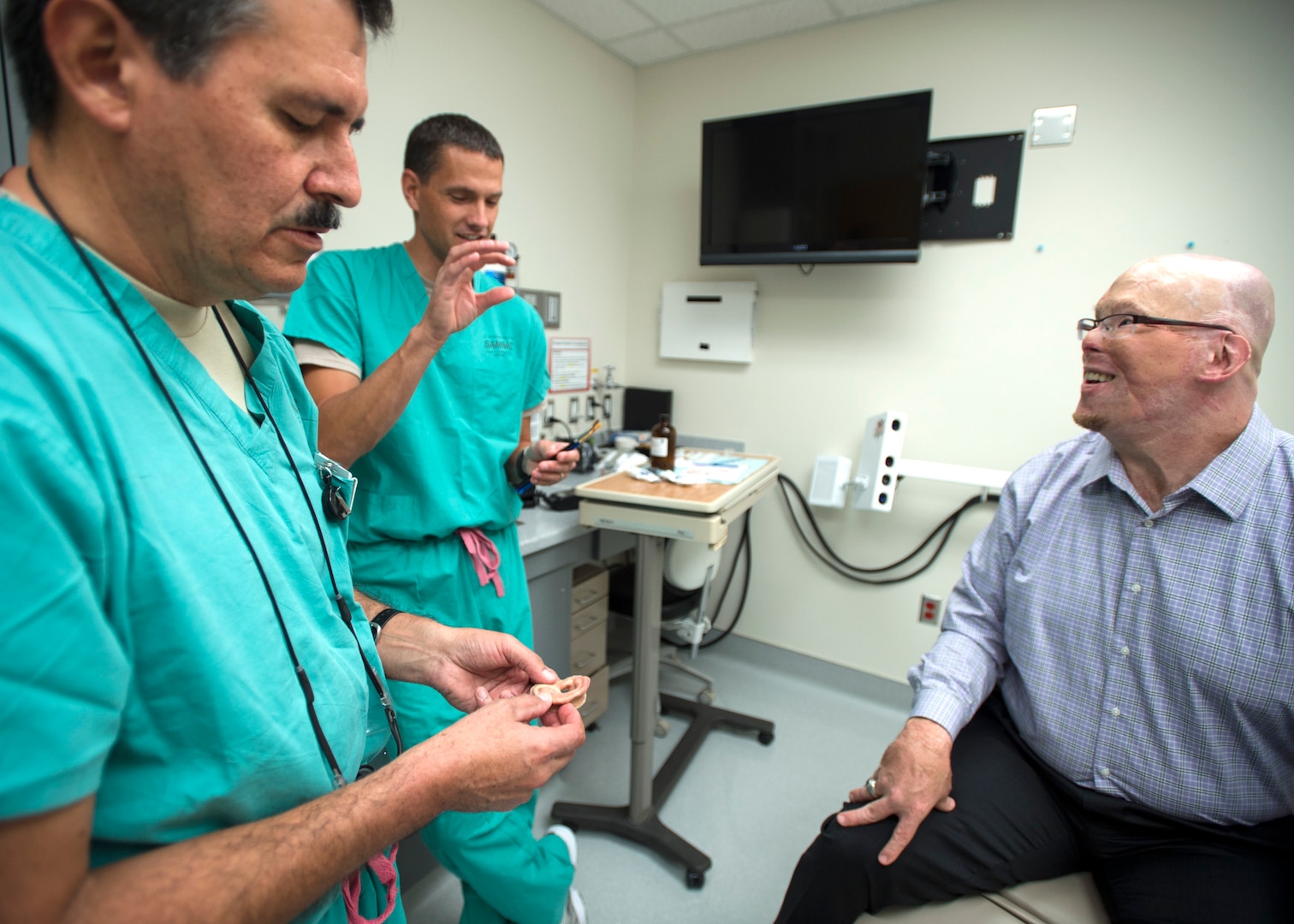 Col. Jose Villalobos (left), 59th Dental Group maxillofacial prosthetics program director, and Maj. Stephen Cherrington (center), 59th Dental Group maxillofacial prosthodontist, discuss retired Army Master Sgt. Todd Nelson’s new prosthetic ear at the San Antonio Military Medical Center, Joint Base San Antonio-Fort Sam Houston, Texas, June 28. The 59th Medical Wing's Maxillofacial Prosthetics Department is one of only a few in the Department of Defense that creates prosthetic body parts, such as eyes, ears and noses. (U.S. Air Force photo/Staff Sgt. Kevin Iinuma)