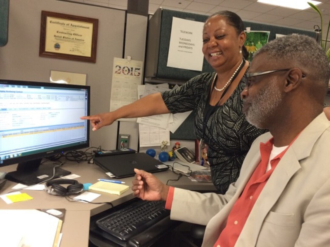 DeVora Seymore, procurement analyst and member of Defense Logistics Agency Aviation’s Contracting Operations Support Team provides desk side assistance to Melvin Green, contracting officer, DLA Aviation’s Bearings Division June 24, 2016. 