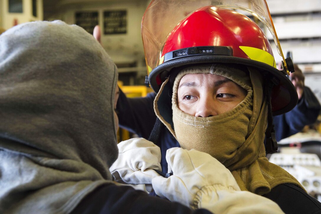 Navy Petty Officer 3rd Class Evelyne Serrano, left, helps Petty Officer 2nd Class Maria Guzman don her firefighting helmet during a fire drill aboard the amphibious assault ship USS Boxer in the Arabian Gulf, July 9, 2016. Serrano and Guzman are machinist mates. Navy photo by Petty Officer 2nd Class Debra Daco