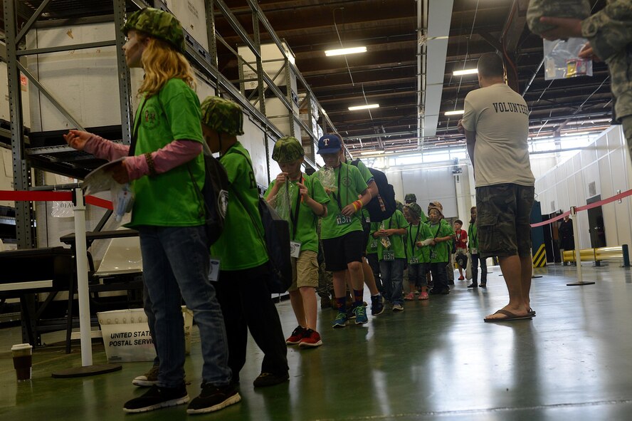 Children process through a simulated deployment line during a Kids Understanding Deployment Operations event July 9, 2016, on McChord Field, Wash. KUDOs included a simulated deployment line; face painting; C-17 Globemaster III static display; and entertaining demonstrations from the JBLM fire department, 22nd Special Tactics Squadron and JBLM explosive ordnance disposal section. (U.S. Air Force photo/Senior Airman Divine Cox)