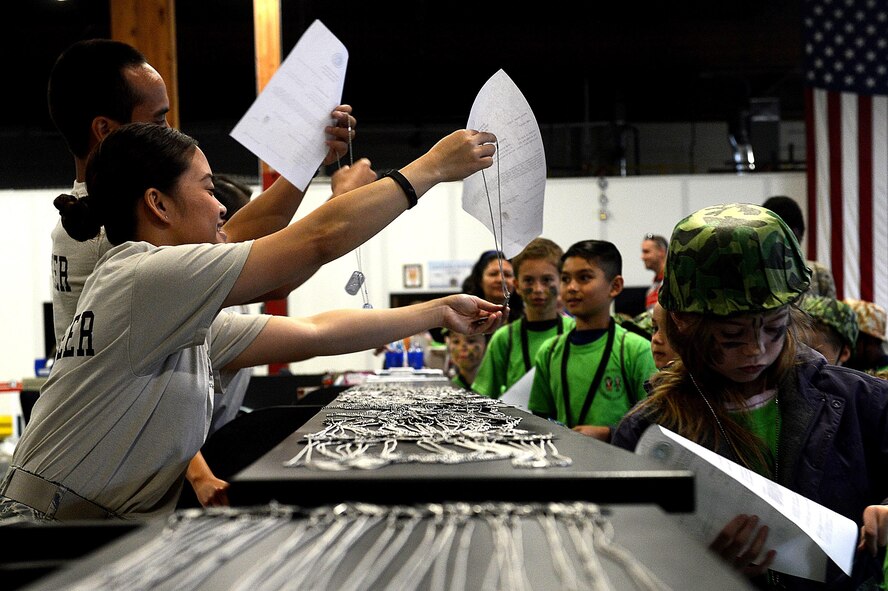 Children receive their dog tags and orders while processing a simulated deployment line during a Kids Understanding Deployment Operations event July 9, 2016, on McChord Field, Wash. The children started the deployment process in groups and proceeded through the processing line where they received helmets, t-shirts, water bottles, resource brochures, dog tags, orders and other equipment for their deployment. (U.S. Air Force photo/Senior Airman Divine Cox)