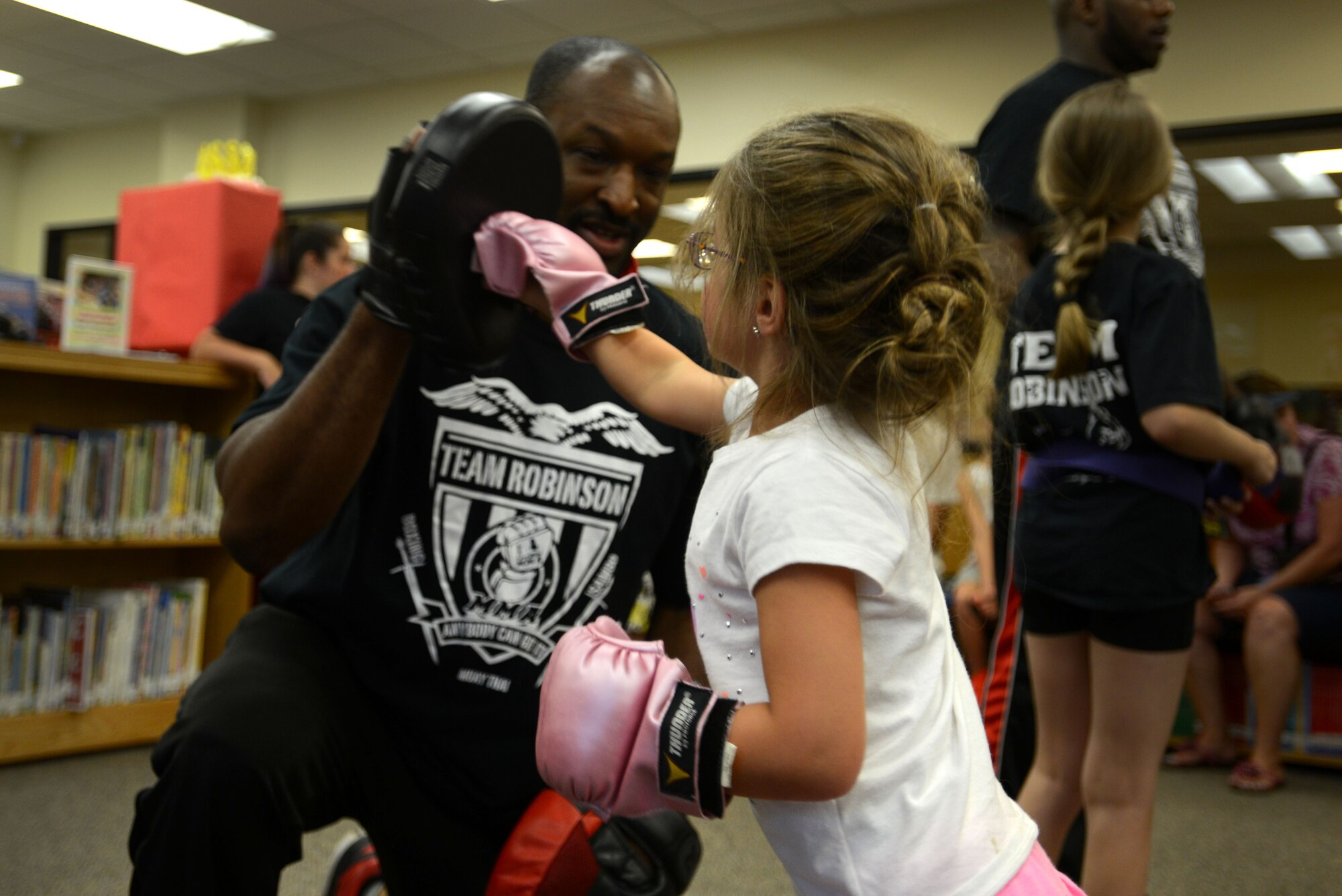 A Team Shaw child hits a glove held by a member of Team Robinson MMA during a summer reading program event at the McElveen Information and Learning Center at Shaw Air Force Base, S.C., June 24, 2016. After learning basic martial arts moves, the children were allowed to put on gloves to participate in drills. (U.S. Air Force photo by Airman 1st Class Kelsey Tucker)