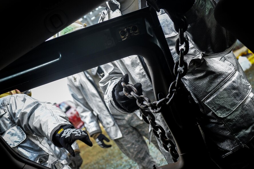 A firefighter from the 2nd Civil Engineer Squadron ties a chain around a vehicle door during an accident victim extraction exercise at Barksdale Air Force Base, La., July 7, 2016. Airmen used chains and other harnesses to secure and guide vehicle doors during removal, promoting safety and reducing risk during the exercise. (U.S. Air Force photo/Senior Airman Mozer O. Da Cunha)
