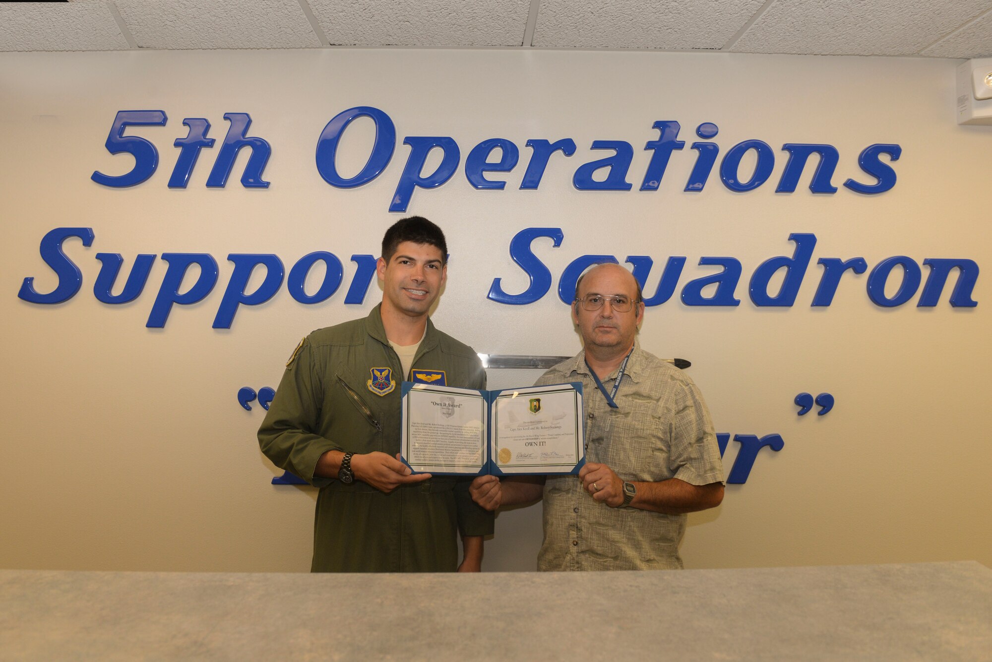 Capt. Alex Kroll and Mr. Robert Seekings, 5th Operations Support Squadron Weapons System Trainer Mission Planning Cell team members, accept the 5th Bomb Wing “Own It Award” at Minot Air Force Base, N.D., July 12, 2016. Kroll and Seekings were awarded for recognizing a critical MPC gap in Secret Internet Protocol Router Network capability and creating a stand-alone MPC function. Kroll and Seekings coordinated with the 5th Communications Squadron and the 5th Civil Engineer Squadron to provide over $20,000 of foundational infrastructure to create this function. (U.S. Air Force Photo/Airman 1st Class Jessica Weissman)