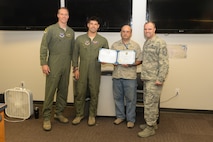 Col. Matthew Brooks, 5th Bomb Wing commander, left, and Chief Master Sgt. Paul Elliott III, 5th BW command chief, right, present an Own-It Award to Capt. Alex Kroll and Mr. Robert Seekings, 5th Operations Support Squadron Weapons System Trainer Mission Planning Cell (MPC) team members, at Minot Air Force Base, N.D., July 12, 2016. Kroll and Seekings were awarded for creating the first stand-alone MPC function. (U.S. Air Force photo/Airman 1st Class Jessica Weissman)