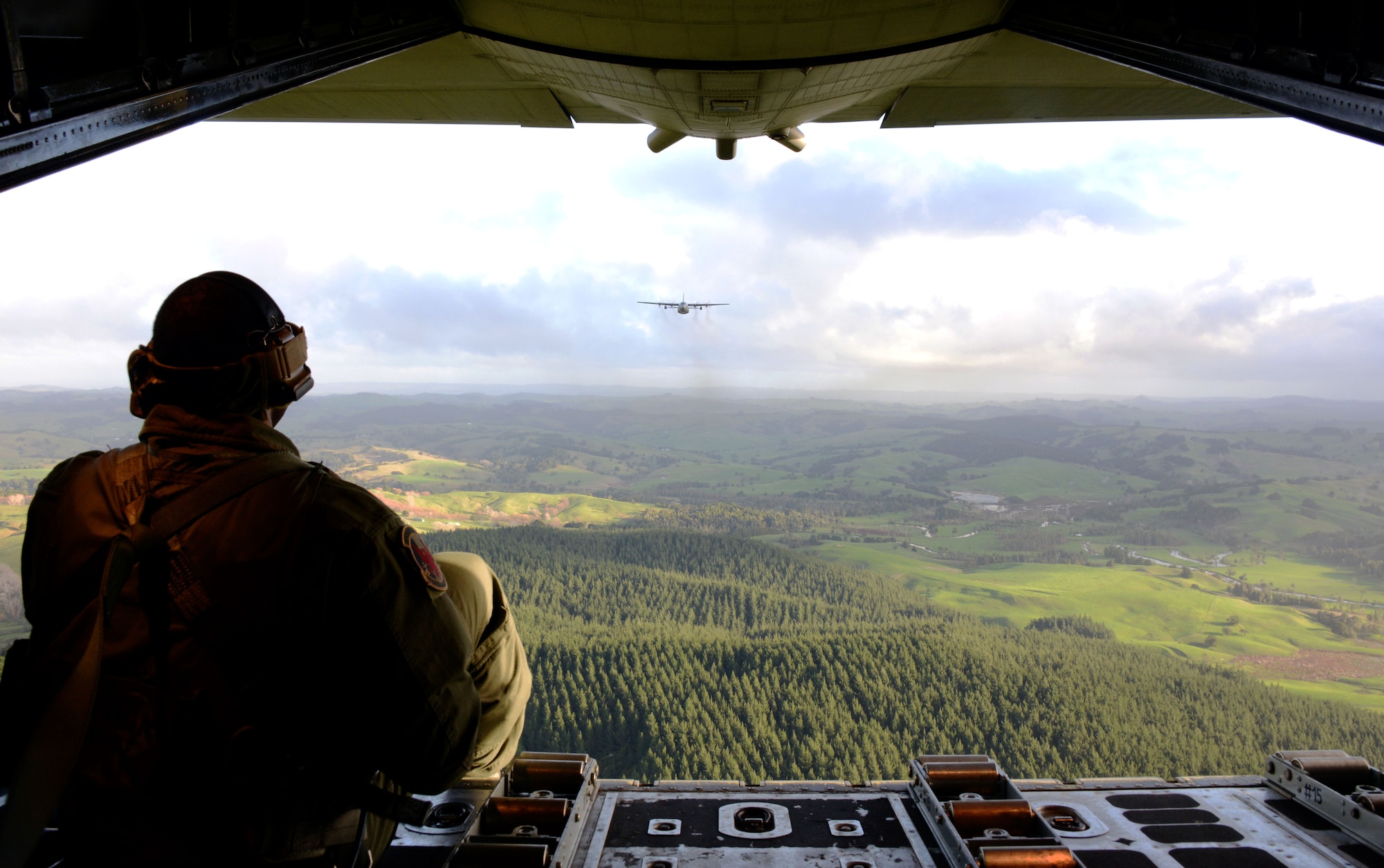 A 1st Special Operations Squadron loadmaster sits on the back of an MC-130H Combat Talon II and watches a Royal New Zealand Air Force C-130 Hercules during a dissimilar formation low level flight June 23, 2016.  Members from the 353rd Special Operations Group participated in Exercise Teak Net June 12 through June 30 in Whenuapai, New Zealand. During the exercise, members from both the New Zealand Defense Force and U.S. Air Force worked together to conduct personnel and equipment air drops together while exchanging new techniques. (U.S. Air Force photo by Master Sgt. Kristine Dreyer)