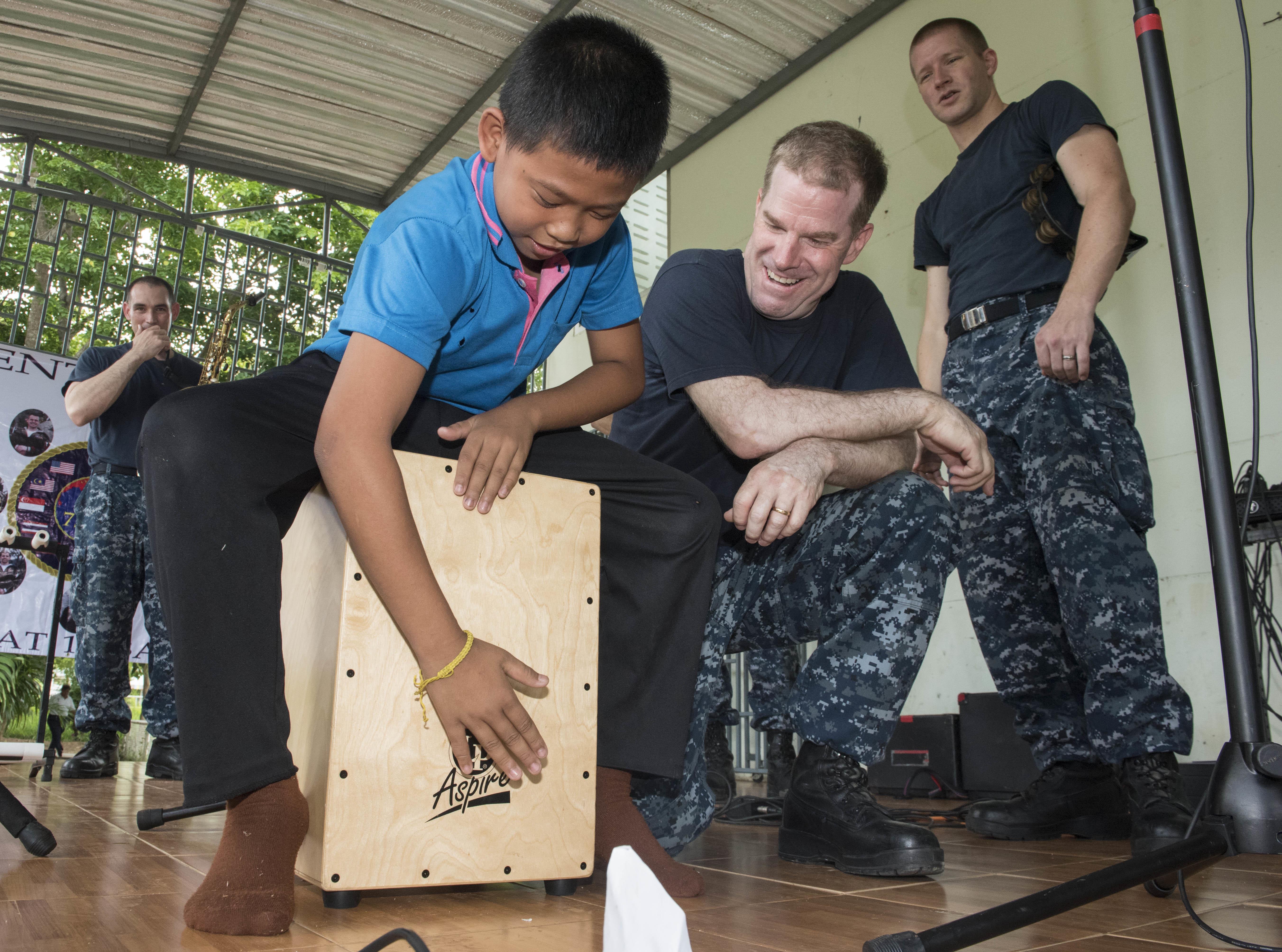 160622-N-OU129-047 SATTAHIP, Thailand (June 22, 2016) The 7th Fleet Rock Band "Orient Express" teaches a student from Chuksamet School how to play a cajon box drum during a concert in support of Cooperation Afloat Readiness and Training (CARAT) Thailand 2016. CARAT is a series of annual maritime exercises between the U.S. Navy, U.S. Marine Corps and the armed forces of nine partner nations to include Bangladesh, Brunei, Cambodia, Indonesia, Malaysia, the Philippines, Singapore, Thailand, and Timor-Leste. (U.S. Navy photo by Mass Communication Specialist 2nd Class Joshua Fulton/Released)