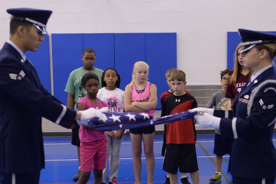 Military children watch Airmen from the base Honor Guard fold the flag during Youth Boot Camp at Minot Air Force Base, N.D., July 7, 2016. Children learned about drill, basic combatives, team-building and survival training during the week-long camp. (U.S. Air Force photo/Airman 1st Class Jessica Weissman)