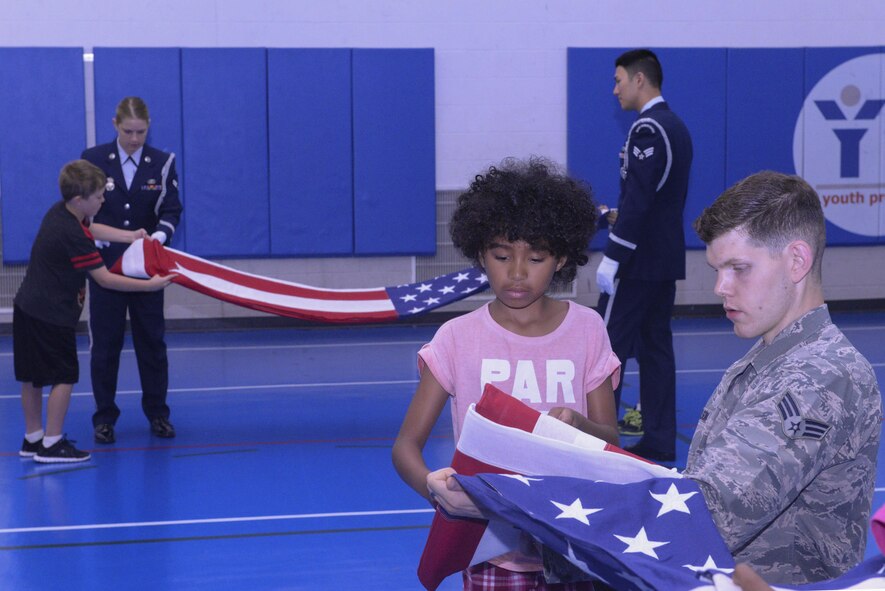 Military children learn how to fold an American flag from the base Honor Guard during Youth Boot Camp at Minot Air Force Base, N.D., July 7, 2016. Youth Boot Camp allowed children to tour a B-52 Stratofortress dock, make a shelter during survival training and shoot paintball guns during target practice. (U.S. Air Force photo/Airman 1st Class Jessica Weissman)