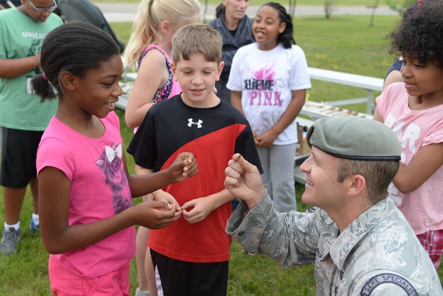 Tech. Sgt. Clifton Cleveland, a Survival, Evasion, Resistance, and Escape specialist assigned to the 5th Operations Support Squadron, eats a cricket with a military child during the Youth Center Boot Camp at Minot Air Force Base, N.D., July 7, 2016. Children were able to build shelter with limited supplies and observe a SERE specialist make fire. (U.S. Air Force photo/Airman 1st Class Jessica Weissman)