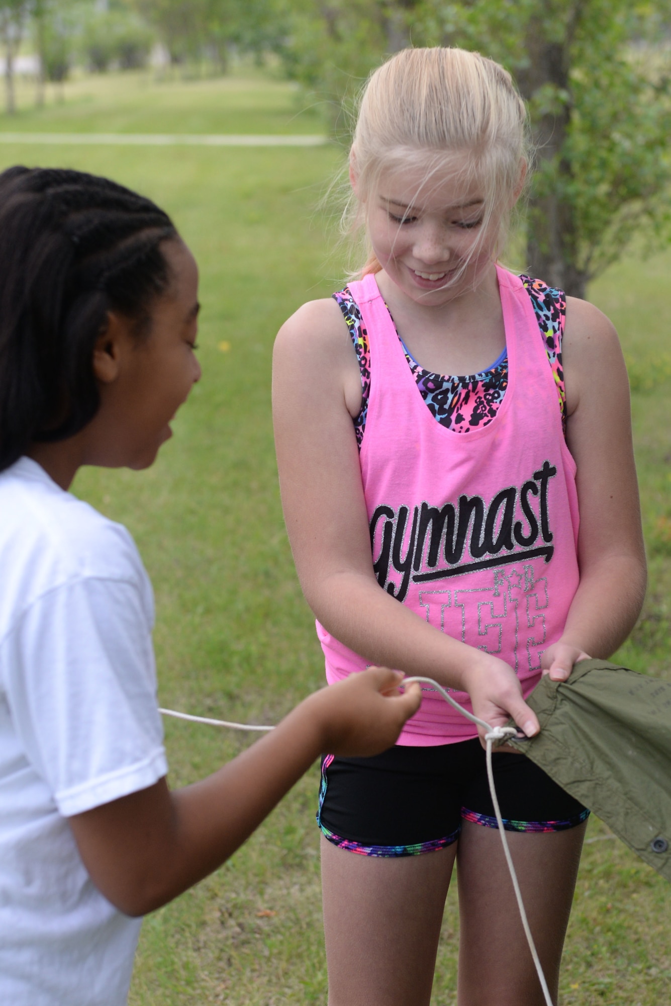 Hannah Schmechel and Janel Fenner tie down a parka to create a make-shift shelter during survival training at the Youth Boot Camp at Minot Air Force Base, N.D., July 7, 2016. Children were able to create a shelter for their team of five using parkas, rope, emergency blankets and sticks. (U.S. Air Force photo/Airman 1st Class Jessica Weissman)