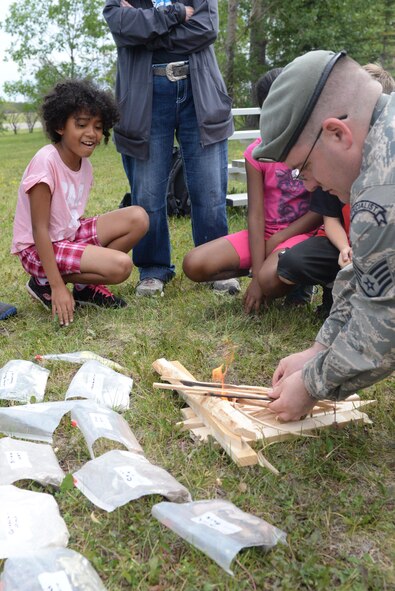 Ariana Montgomery watches as Staff Sgt. Anthony Barrette, a Survival, Evasion, Resistance and Escape specialist assigned to the 5th Operations Support Squadron, creates fire during Youth Boot Camp at Minot Air Force Base, N.D., July 7, 2016. Children learned the importance of warmth, food and water during a simulated survival situation. (U.S. Air Force photo/Airman 1st Class Jessica Weissman)