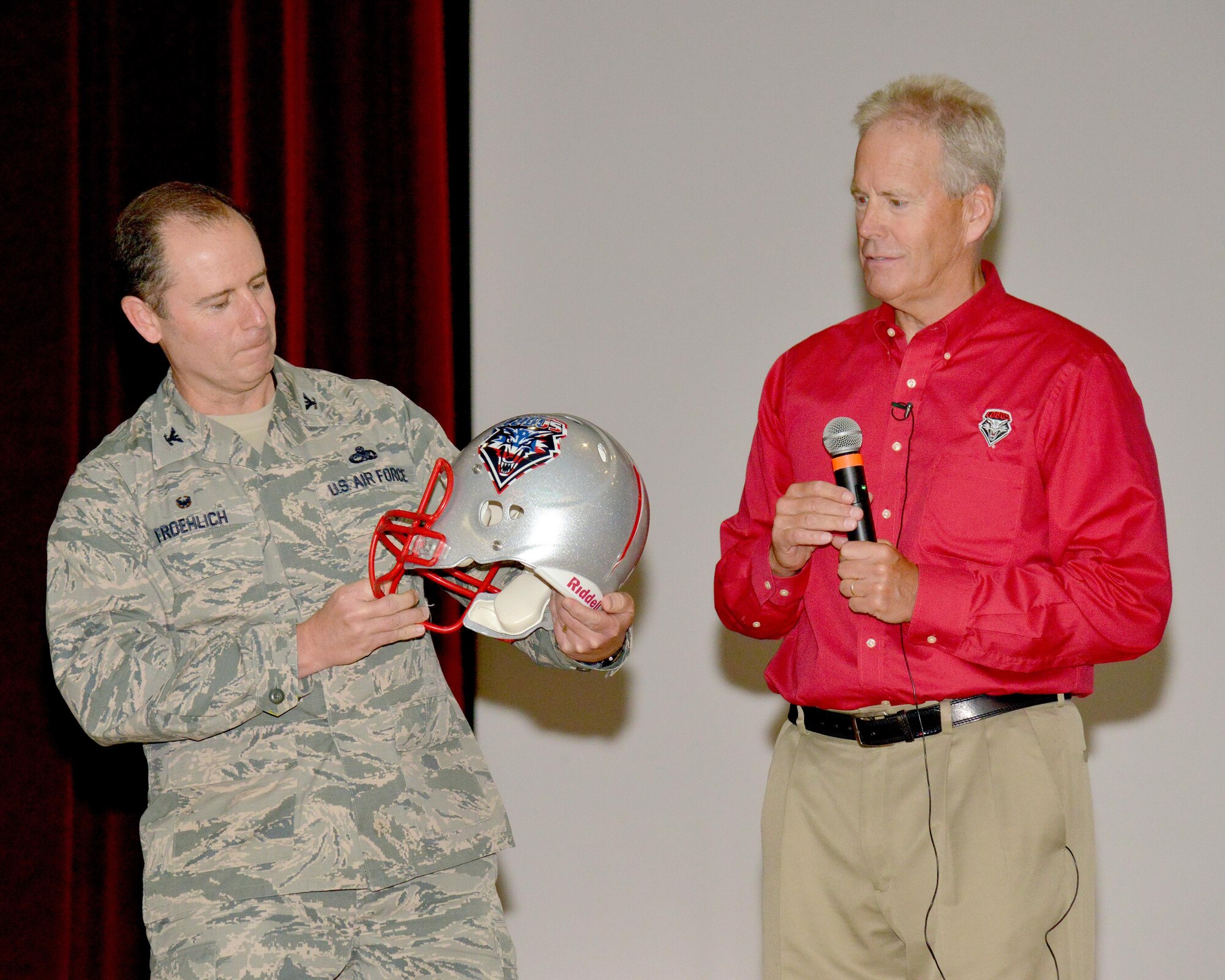 Bob Davie, head coach of the University of New Mexico football team, presents a team helmet to Col. Eric Froehlich, 377th Air Base Wing commander, following a presentation at the Base Theater July 8. Davie spoke to Airmen and other Kirtland workers about leadership and the importance of having good responses to challenging events.  (Photo by Jamie Burnett)