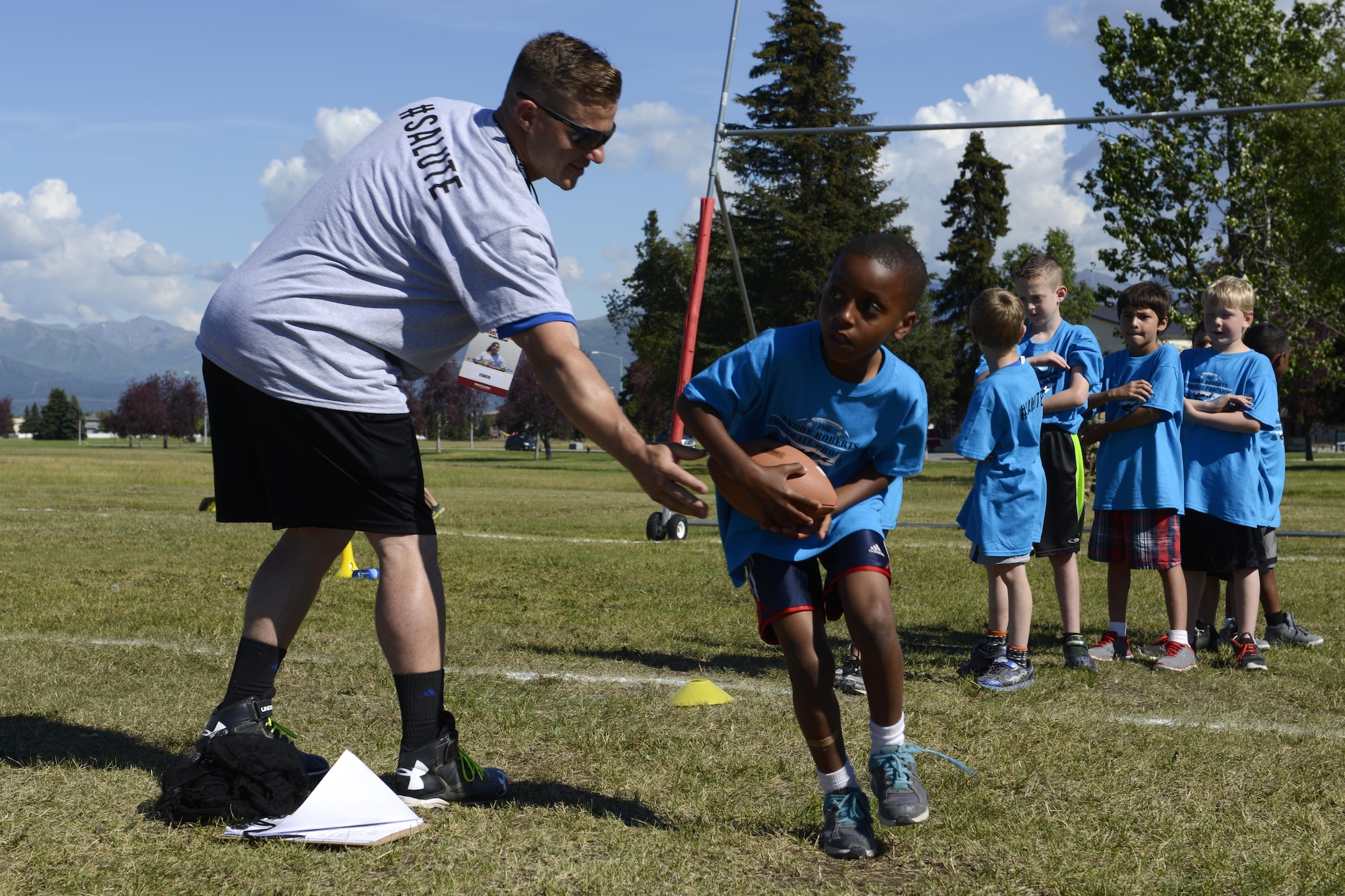 Steven Peaper, 673d Air Base Wing PME instructor, hands off a football to a Joint Base Elmendorf-Richardson athlete at the Military ProCamp at JBER, Alaska, June 12, 2016. More than 130 JBER youth, ranging from first to eight grade attended the event. (U.S. Air Force photo by Airman 1st Class Javier Alvarez)