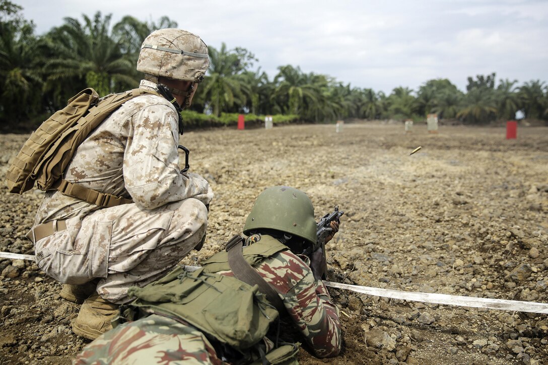Lance Cpl. Christopher Parsons, a rifleman with Special Purpose Marine Air-Ground Task Force Crisis Response-Africa, watches a Cameroonian soldier with Forces Fusiliers Marins et Palmeurs de Combat shoot their weapon on the range in Limbé, Cameroon, July 1, 2016.  Marines share tactics, techniques and skills with the FORFUMAPCO soldiers to combat the illicit trafficking in Cameroon.