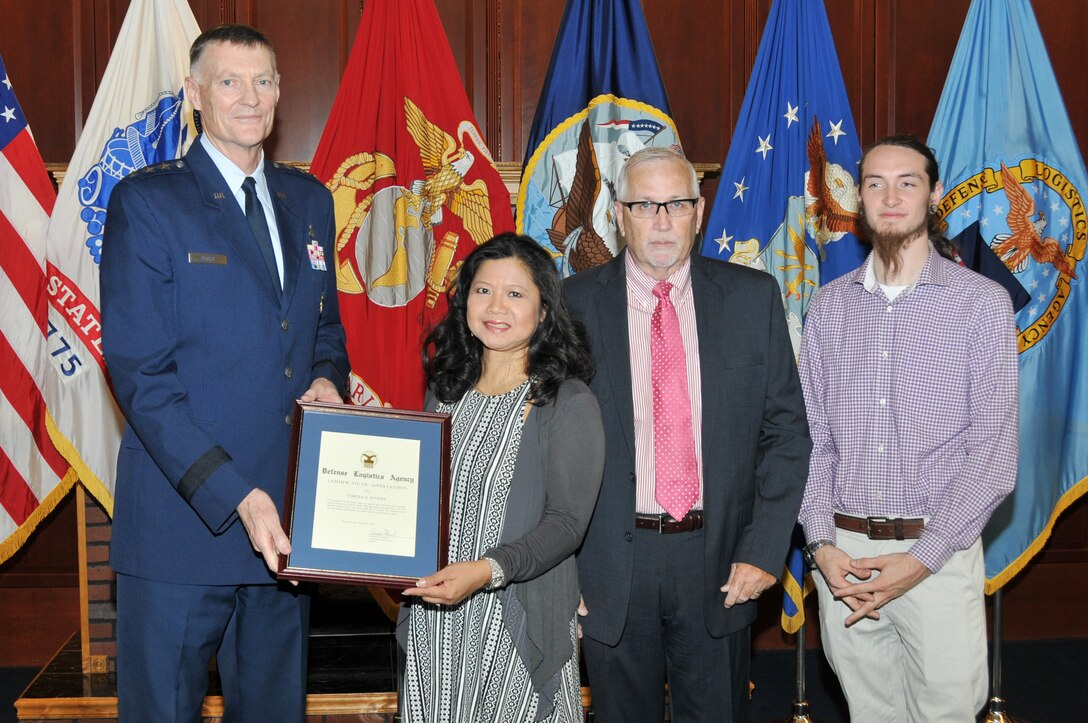 DLA Director Air Force Lt. Gen. Andy Busch (far left) presents an award to Air Force Lt. Col. Teresa Rivers for supporting her husband, Randy Taft (second from right) in his career  as son Cody Taft (far right) looks on.