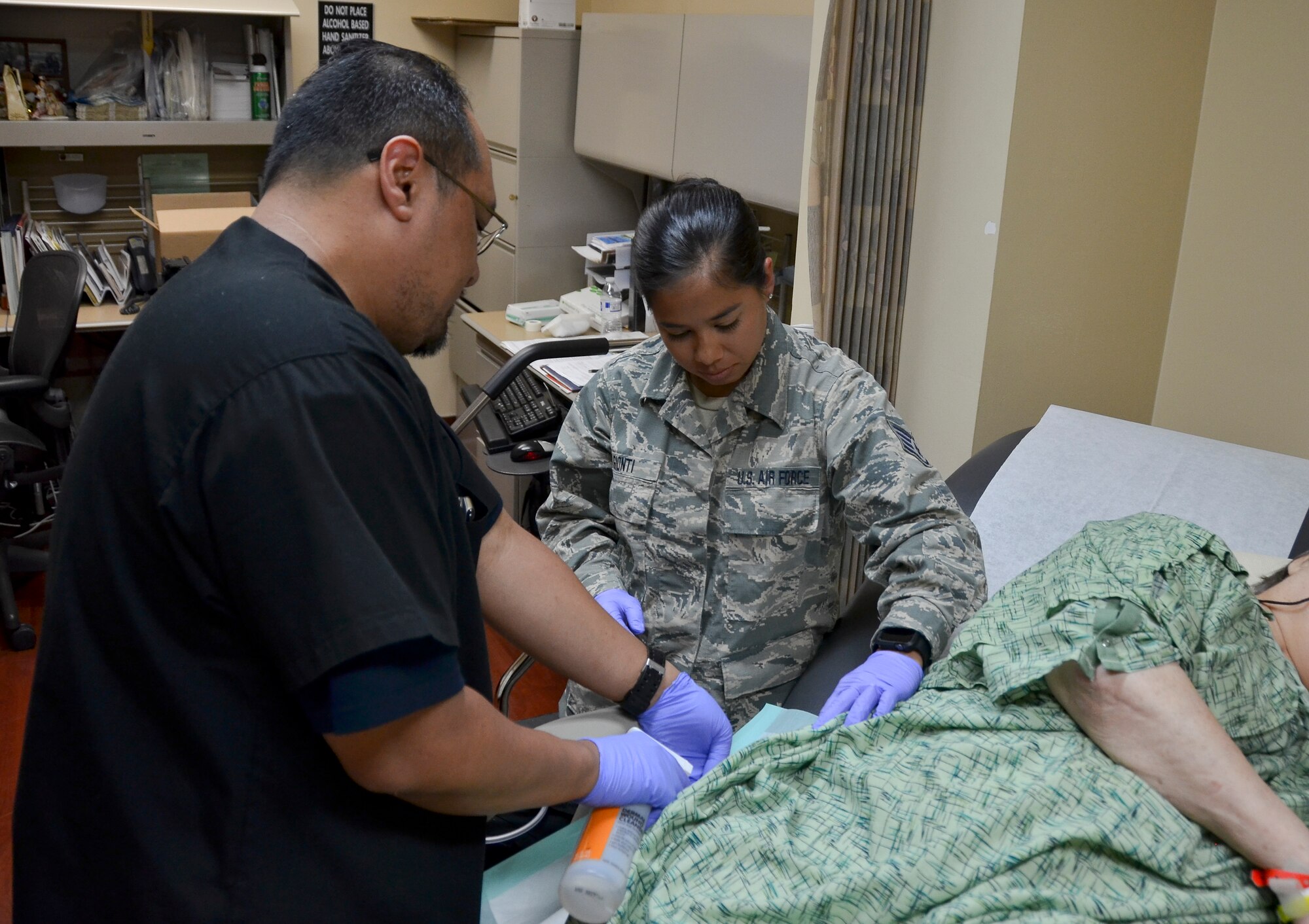 Rodrigo Bautista, health technician (near), Naval Medical Center San Diego, and Staff Sgt. Megan Gionti, medical technician, 117th Medical Group, sanitize a patient's wound in the Naval Medical Center San Diego Wound Care Clinic, in San Diego, Calif., June 27, 2016.  The 117 MDG trained with the U.S. Navy at Naval Medical Center San Diego.  The training included Airmen being implemented in real world U.S. Naval operations.  (U.S. Air National Guard photo by Staff Sgt. Jeremy Farson/Released)   