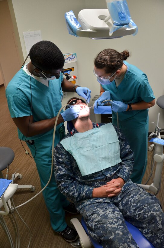 Lt. Webster K. Felix (left), general dentist, Naval Branch Health Clinic, Naval Base San Diego, and Airman 1st Class Chayce Shelton, dental technician, 117th Medical Group, provide dental care to a patient in the clinic, in San Diego, Calif., June 23, 2016.  The 117 MDG trained with the U.S. Navy at Naval Medical Center San Diego.  The training included Airmen being implemented in real world U.S. Naval operations.  (U.S. Air National Guard photo by Staff Sgt. Jeremy Farson/Released)   