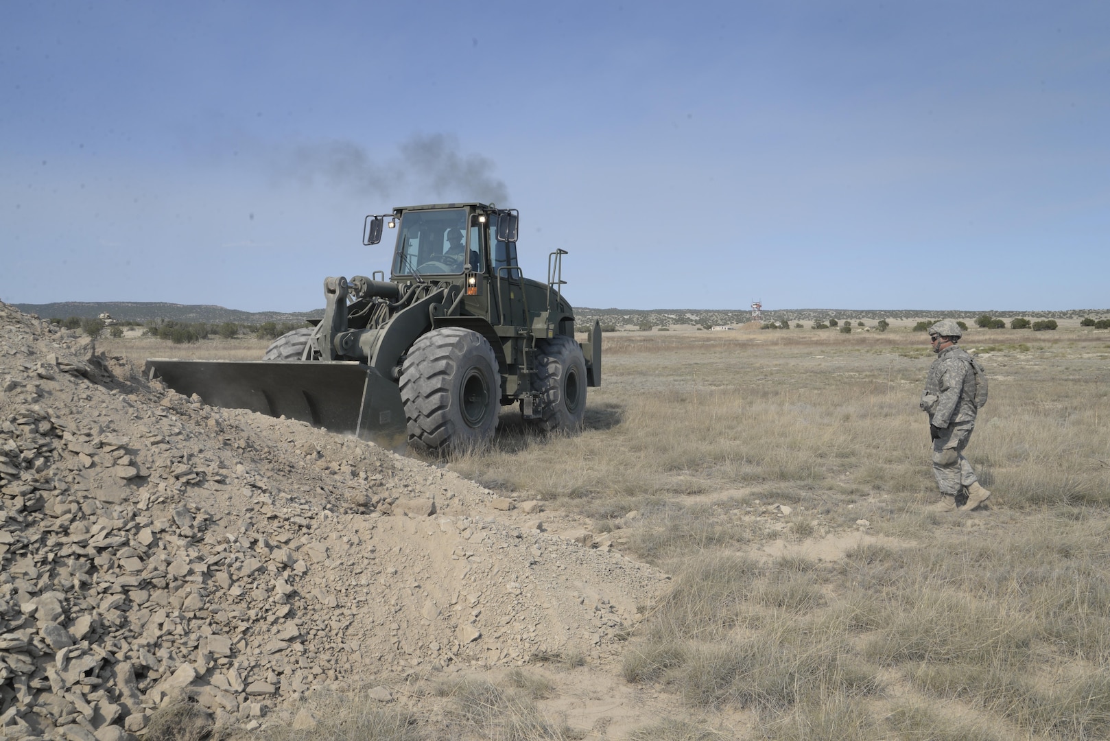 Private 2nd Class Blake Burtzlaff, horizontal construction engineer, directs a front-loader operated by Spc. Jacob Lane, horizontal construction engineer, both of 842nd Engineer Company, 153rd Engineer Battalion, 196th Maneuver Enhancement Brigade, South Dakota National Guard, July 12, 2015, at the Fort Carson Pinon Canyon Maneuver Site, during the Iron Strike field training exercise conducted by 3rd Armored Brigade Combat Team, 4th Infantry Division, from July 7-22.