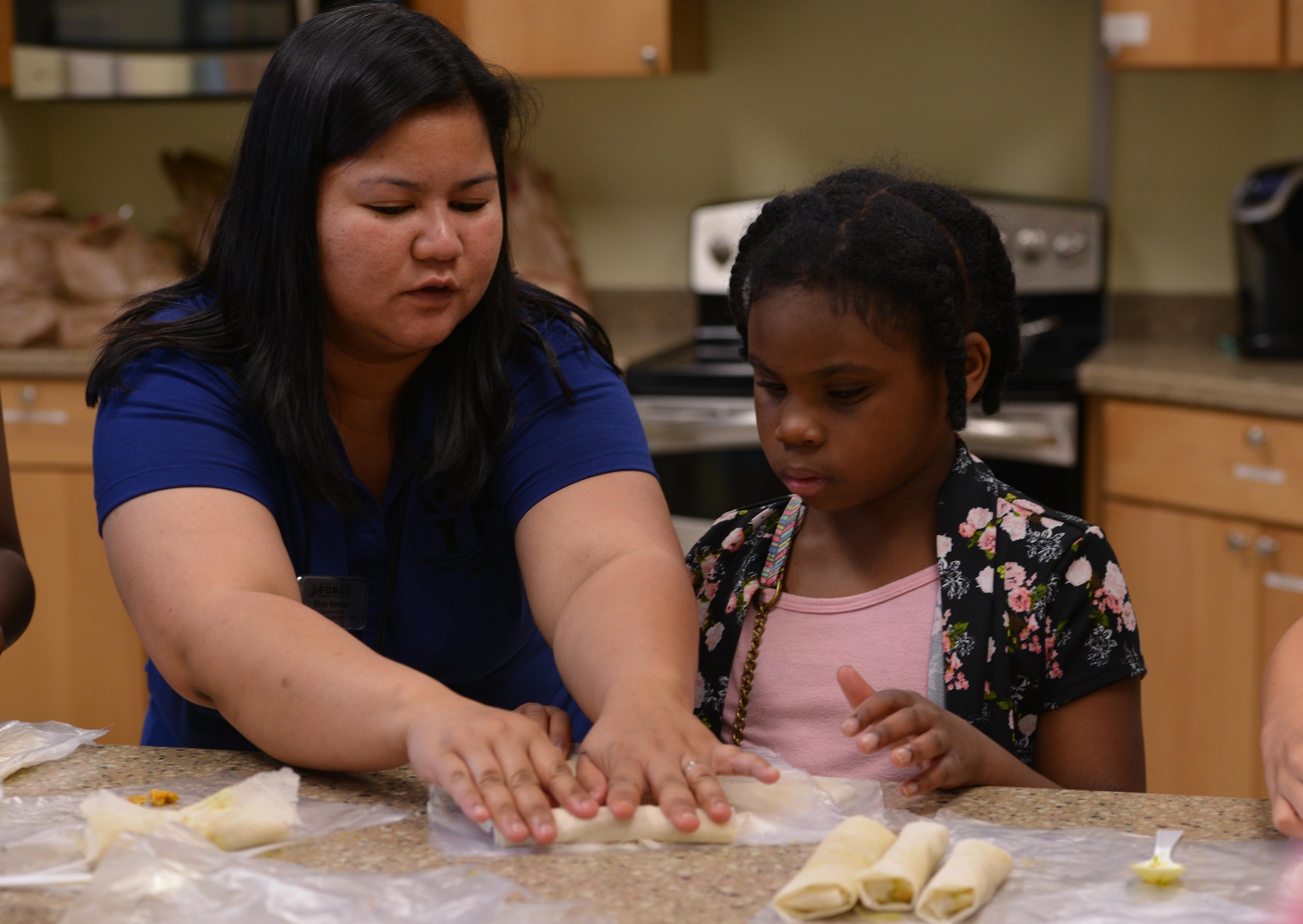 Elida Narciso, an operations clerk at Two Rivers Youth Center, assists Amira Ball, 10, roll an egg roll at the Two Rivers Cooking Camp hosted at Joint Base Elmendorf-Richardson, Alaska, July 11, 2016. According to author Andrew Coe, who wrote “Chop Suey: A Cultural History of Chinese Food in the United States,” the egg roll was likely invented in New York sometime in the early 1930s. (U.S. Air Force photo by Airman 1st Class Javier Alvarez)