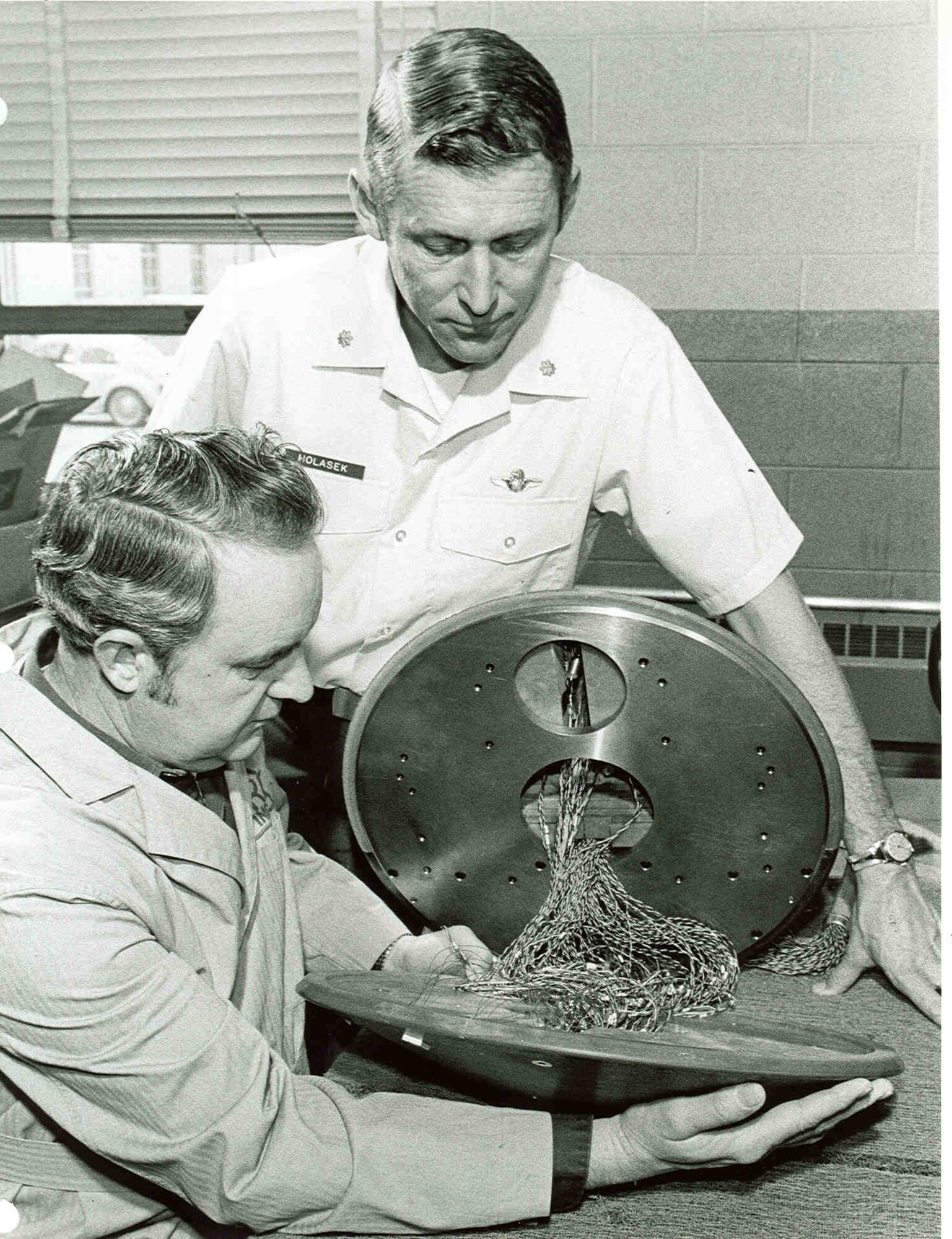 Extensive instrumentation required on the NASA Viking model is shown here before a test at AEDC in 1973 before final assembly. There were 68 sensors to record localized heat buildup around protrusions on the face of the Mars entry vehicle, while 13 heat and five pressure sensors were installed on the base cover. Then Maj. Dale Holasek of the AEDC Directorate of Test watches the assembly by Ray Moore, a test facility craftsman. (AEDC photo)