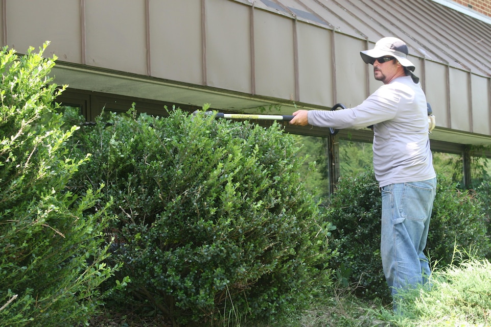 An employee of Facilities Maintenance Section Shop 71, which is in charge of maintaining roads and grounds aboard Marine Corps Base Quantico, trims hedges in front of Newlin Hall on a black-flag weather condition day, July 7.