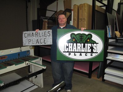 Wes Atkinson, Naval Consolidated Brig Charleston's sign shop supervisor, holds up the old and new Charlie’s Place sign. (Courtesy photo) 