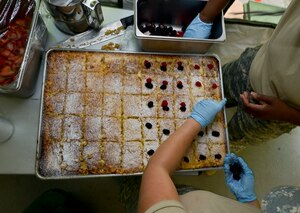 U.S. Army Reserve Soldiers with the Echo Company, 5th Battalion, 159th General Support Aviation Brigade, top a cake with fruit and powdered sugar at Fort Eustis, Va., July 13, 2016.  The Soldiers made the cake as part of a training meal in preparation for an Army-wide culinary competition. (U.S. Air Force photo by Staff Sgt. Natasha Stannard) 
