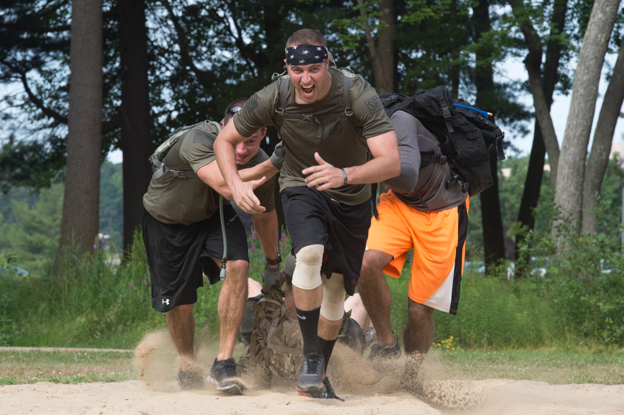 Tech. Sgt. Matthew Marquart, center, 66th Security Forces Squadron Combat Arms NCO in charge, runs across a sand pit as Staff Sgt. Meldion Shehu, left, 66 SFS training NCO, and others participate in a Team Cohesion Challenge on base July 15. Approximately 30 members of the base community participated in the event that is built around special operations training and is designed to teach leadership, promote unit cohesion and inspire teams to perform their best. (U.S. Air Force photo by Jerry Saslav)