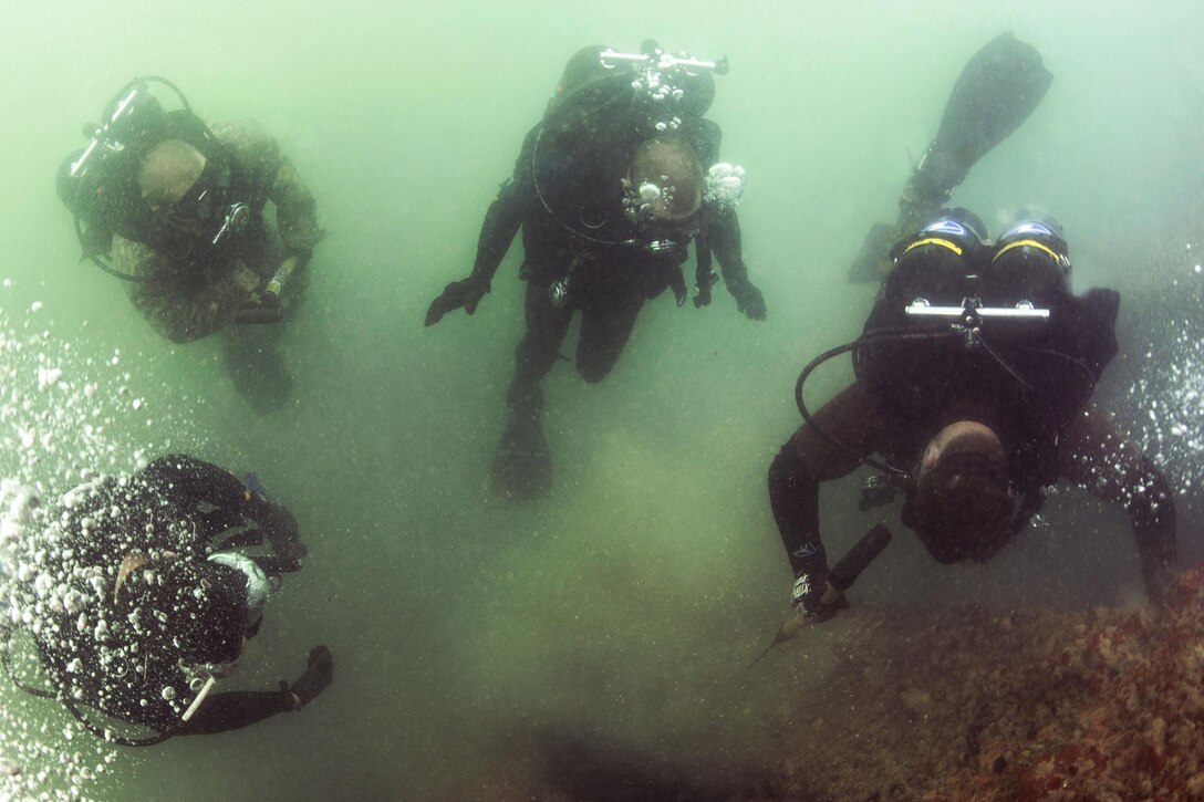 Navy Petty Officer 2nd Class Dan Lehne, right, demonstrates to U.S. and Australian divers how to scrape marine growth from a pile during pier maintenance training led by Navy Underwater Construction Team 2 as part of Rim of the Pacific 2016 at Joint Base Pearl Harbor-Hickam, Hawaii, July 12, 2016. Lehne is a construction electrician assigned to Underwater Construction Team 2. Navy photo by Petty Officer 1st Class Charles E. White