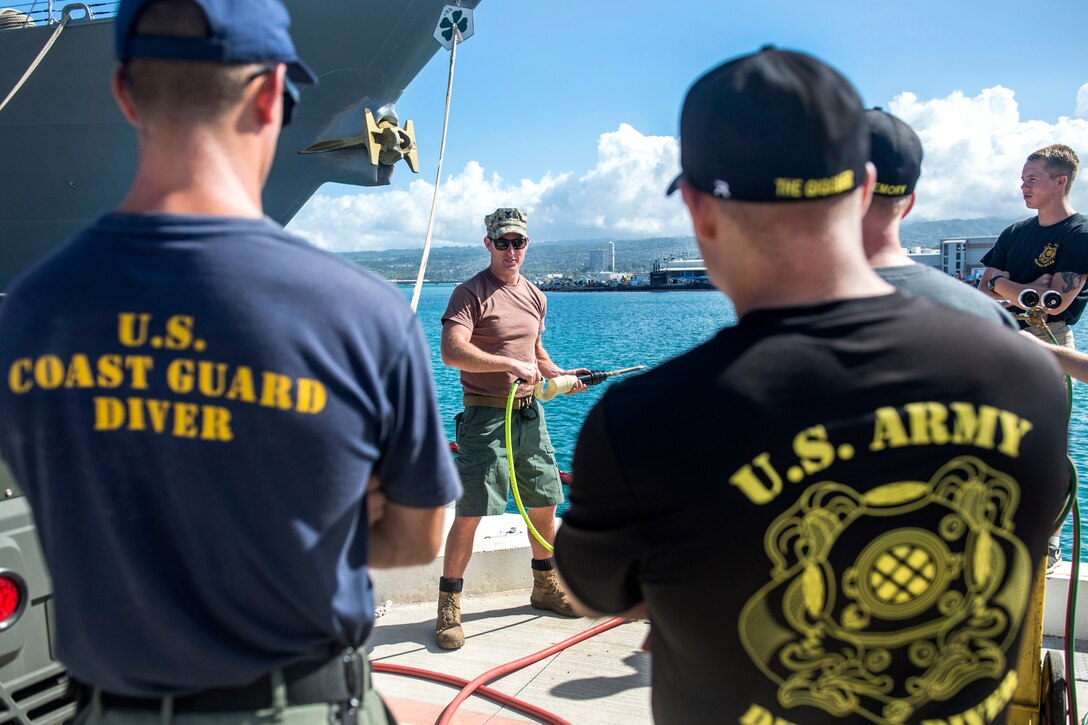 Navy Petty Officer 1st Class Jesse Hamblin, center, explains how to operate a pneumatic demolition hammer to Army and Coast Guard divers during a pier maintenance training mission as part of Rim of the Pacific 2016 at Joint Base Pearl Harbor-Hickam, Hawaii, July 12, 2016. Hamblin is a steelworker assigned to Underwater Construction Team 2, which led the training mission. Navy photo by Petty Officer 1st Class Charles E. White