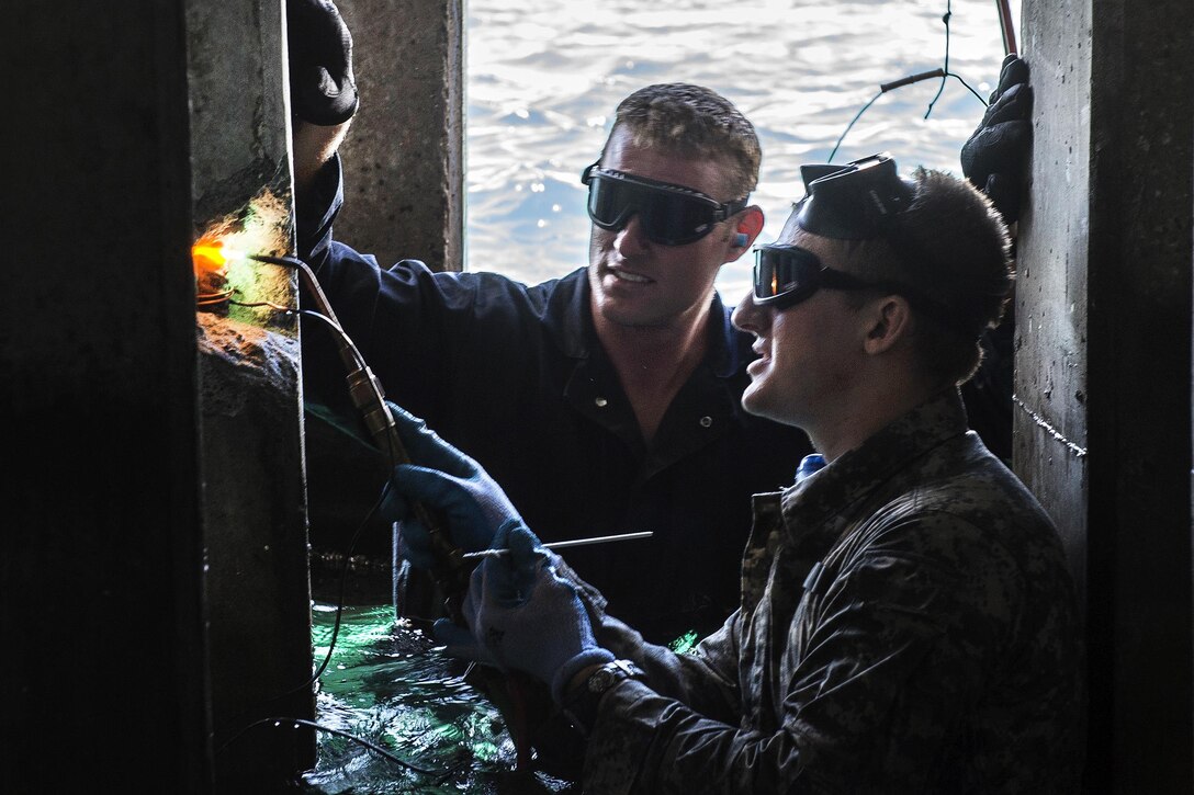 Navy Petty Officer 1st Class Jesse Hamblin, left, observes as Army Pfc. Timothy Sparks brazes a wire to exposed rebar during a pier maintenance training mission as part of Rim of the Pacific 2016 at Joint Base Pearl Harbor-Hickam, Hawaii, July 12, 2016. Hamblin is a steelworker assigned to Underwater Construction Team 2, which led the training. Navy photo by Petty Officer 1st Class Charles E. White