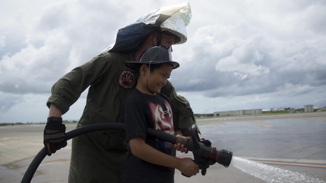 Lance Cpl. Duston Haggard helps an Okinawa elementary school student operate a hand line, also known as a fire hose, July 18 during a tour of Marine Corps Air Station Futenma, Okinawa, Japan. The tour strengthened the bilateral relationship between Marines and Okinawa residents by allowing them to see what Marines do on a daily basis and their day-to-day responsibilities in the workplace. During the visit, guests enjoyed a meal at the Habu Pit, toured the mess hall and explored various static displays on the flight line. Haggard is an aircraft rescue and fire fighting specialist with Headquarters and Headquarters Squadron, Marine Corps Air Station Futenma.