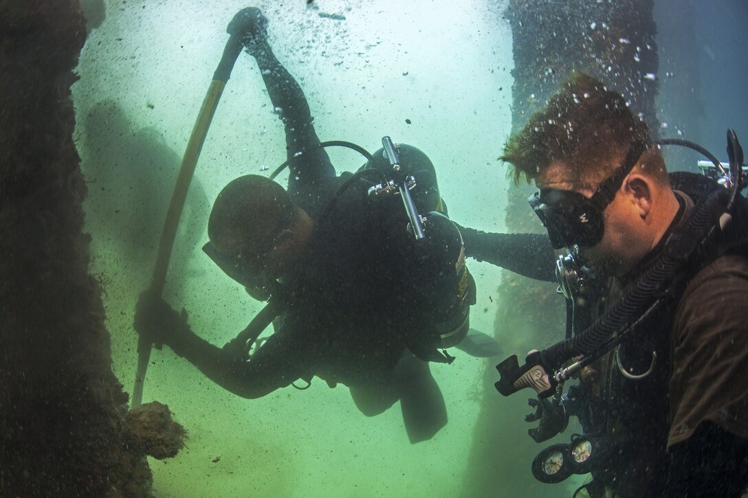 U.S. and Australian divers use a bar to remove marine growth from a pile during pier maintenance training led by Navy Underwater Construction Team 2 as part of Rim of the Pacific 2016 at Joint Base Pearl Harbor-Hickam, Hawaii, July 12, 2016. Navy photo by Petty Officer 1st Class Charles E. White