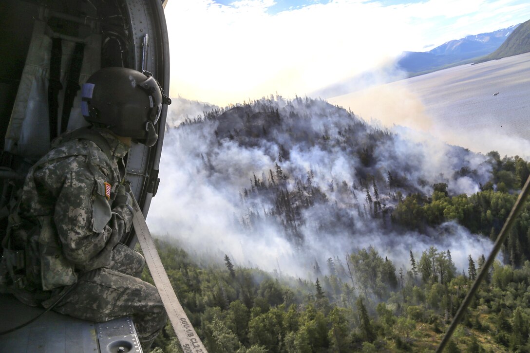 Army Sgt. Adam Weber looks out the side door of a UH-60 Black Hawk helicopter supporting response efforts to the McHugh Creek Fire near Anchorage, Alaska, July 20, 2016. Weber is a crew chief assigned to the Alaska Army National Guard’s Company A, 1st Battalion, 207th Aviation Regiment. Army National Guard photo by Staff Sgt. Balinda O’Neal Dresel