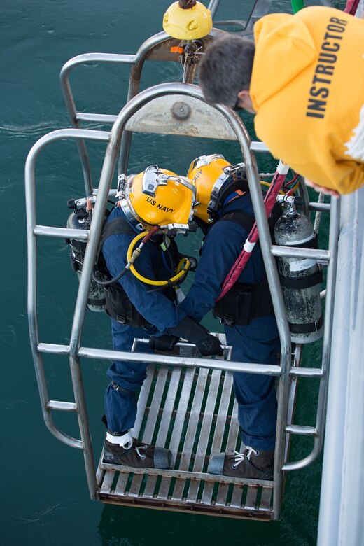 Navy Master Chief Petty Officer Richard Panaccione, an instructor at the Naval Diving and Salvage Training Center, observes two Navy divers as they enter the water from the yard diving tender Poseidon during a surface supplied dive supervisor training evolution, Feb. 18, 2014. Navy photo by Petty Officer 2nd Class Kevin B. Gray