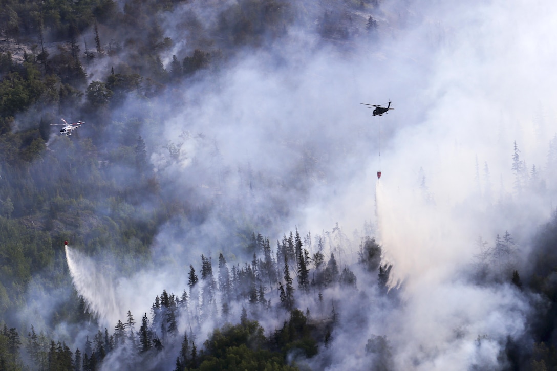 An Army UH-60 Black Hawk helicopter and a civilian helicopter drop water from their bucket firefighting systems while assisting in the response to the McHugh Creek Fire near Anchorage, Alaska, July 20, 2016. Army National Guard photo by Staff Sgt. Balinda O’Neal Dresel