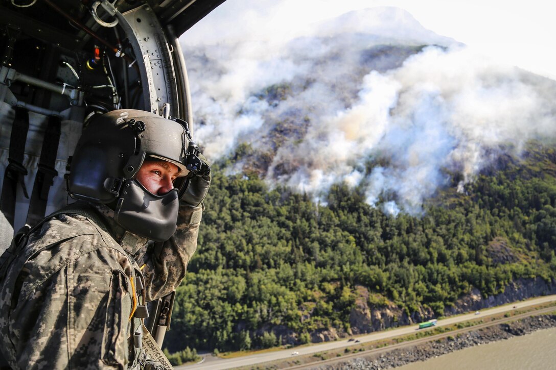 Army Sgt. Adam Weber looks out the side door of a UH-60 Black Hawk helicopter before refilling a bucket firefighting system in Cook Inlet while assisting in the response to the McHugh Creek Fire near Anchorage, Alaska, July 20, 2016. Weber is a crew chief assigned to the Alaska Army National Guard’s Company A, 1st Battalion, 207th Aviation Regiment. Army National Guard photo by Staff Sgt. Balinda O’Neal Dresel