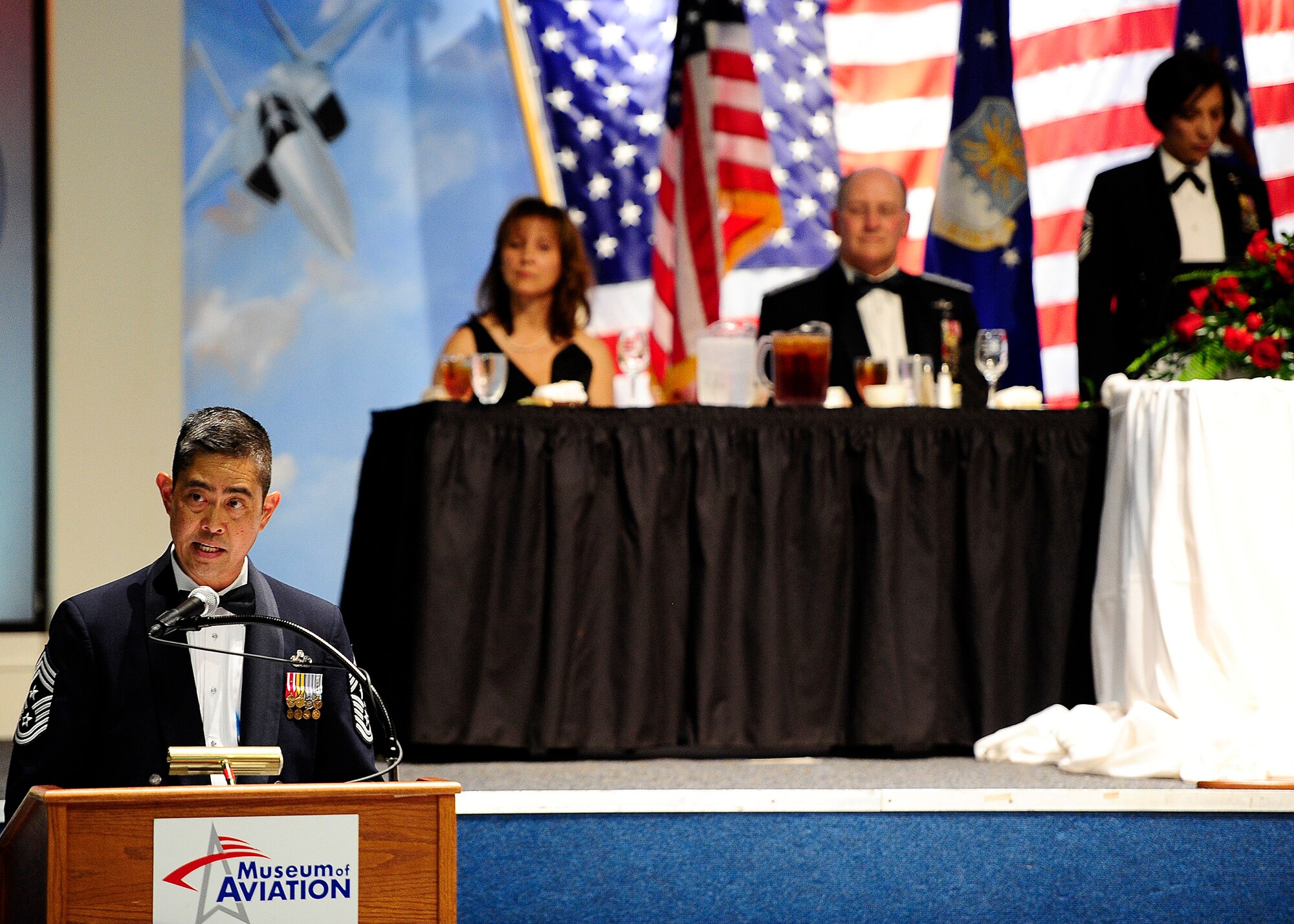 Command Chief of the 4th Air Force, Chief Master Sgt. Brian Wong, performs the duties of the First Sergeant for the Order of the Sword ceremony in honor of former Chief of Air Force Reserve Command Lt. Gen. James F. Jackson in the background along with his wife and Chief Master Sgt. of the Mess Ericka Kelly at the Museum of Aviation in Warner Robins, Ga., July 13, 2016. The Order of the Sword is an honor awarded by the NCOs of a command to recognize individuals they hold in high esteem and for their contributions to the enlisted corps. (U.S. Air Force photo by Tech. Sgt. Stephen D. Schester)